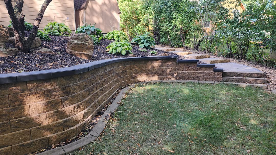 Landscape featuring a curved stone retaining wall and lush greenery in a residential yard.