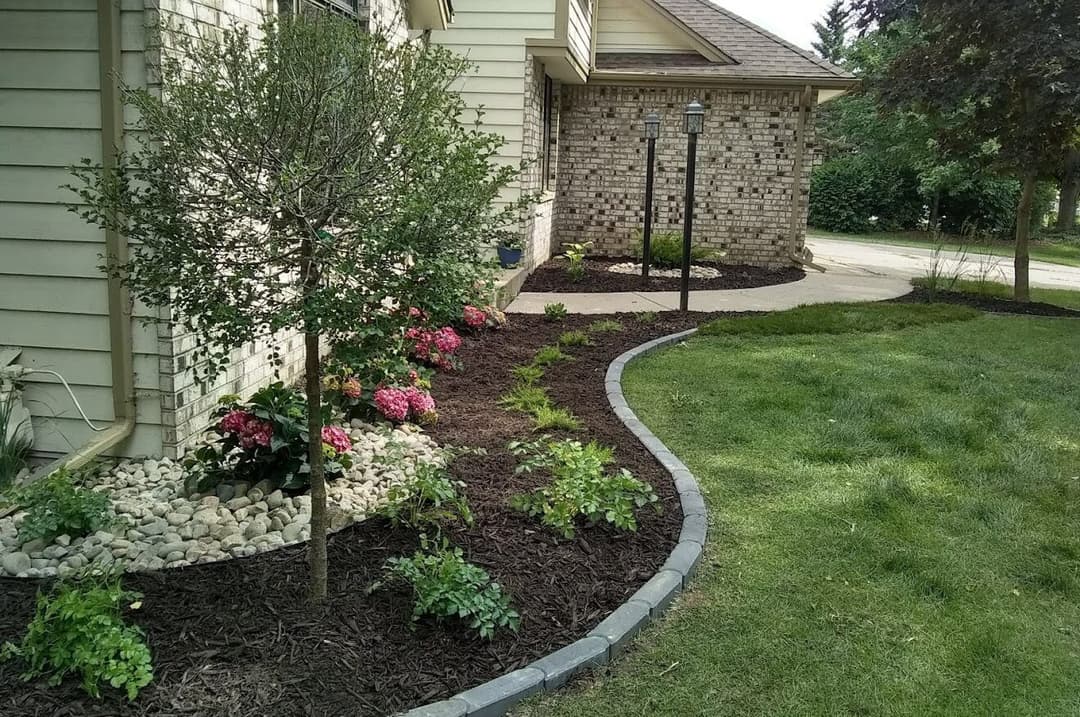 Lush landscaping with pink flowers, mulch, and decorative rocks along a home's exterior.