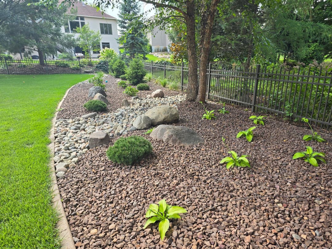 Landscaped garden featuring rocks, shrubs, and hostas along a decorative fence.