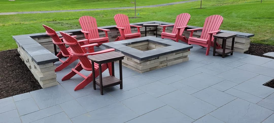 Cozy outdoor seating area with red Adirondack chairs and a stone fire pit on a patio.