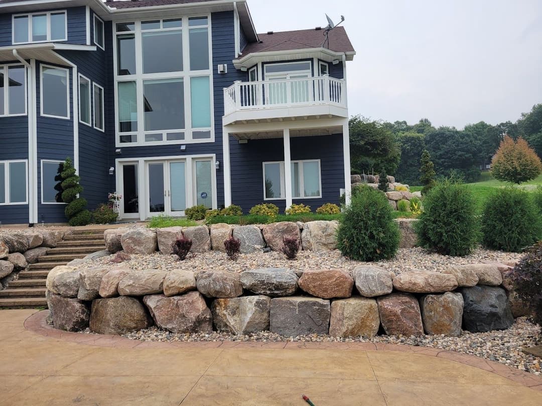 Modern blue house with stone landscaping and lush greenery in a serene outdoor setting.