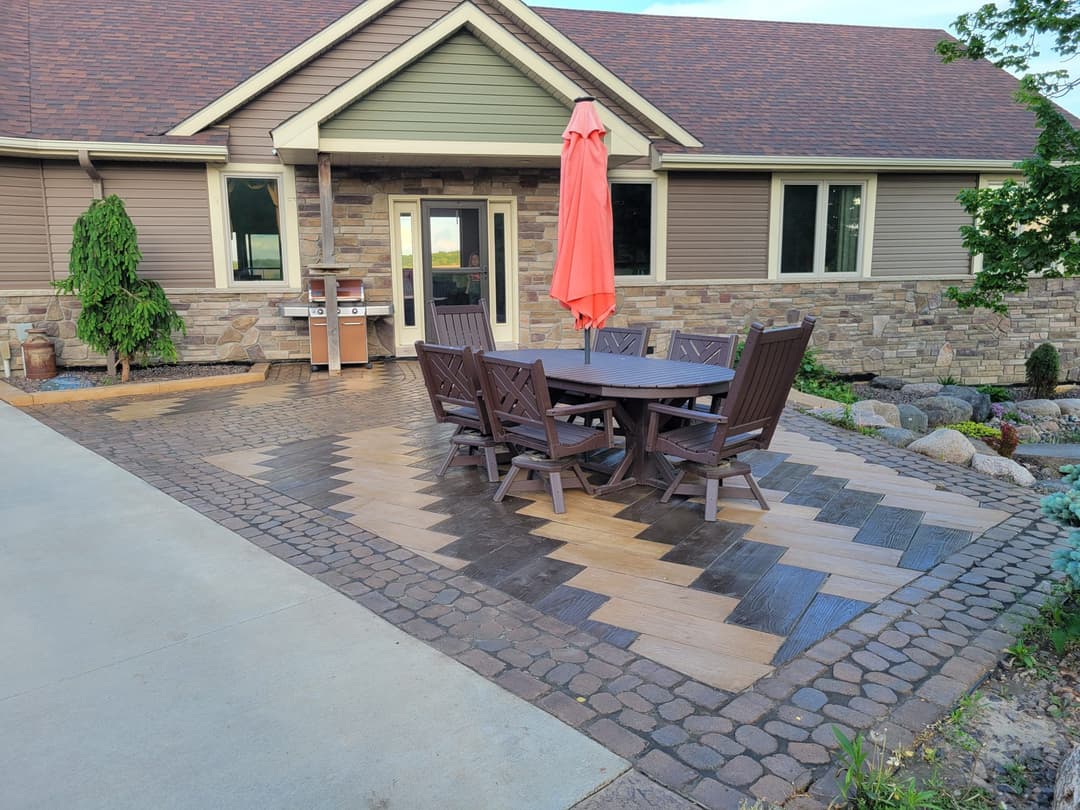 Outdoor patio with wooden table, chairs, umbrella, and stone landscaping. Perfect for gatherings.