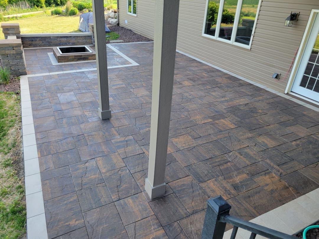 spacious outdoor patio with textured stone flooring and fire pit, surrounded by greenery