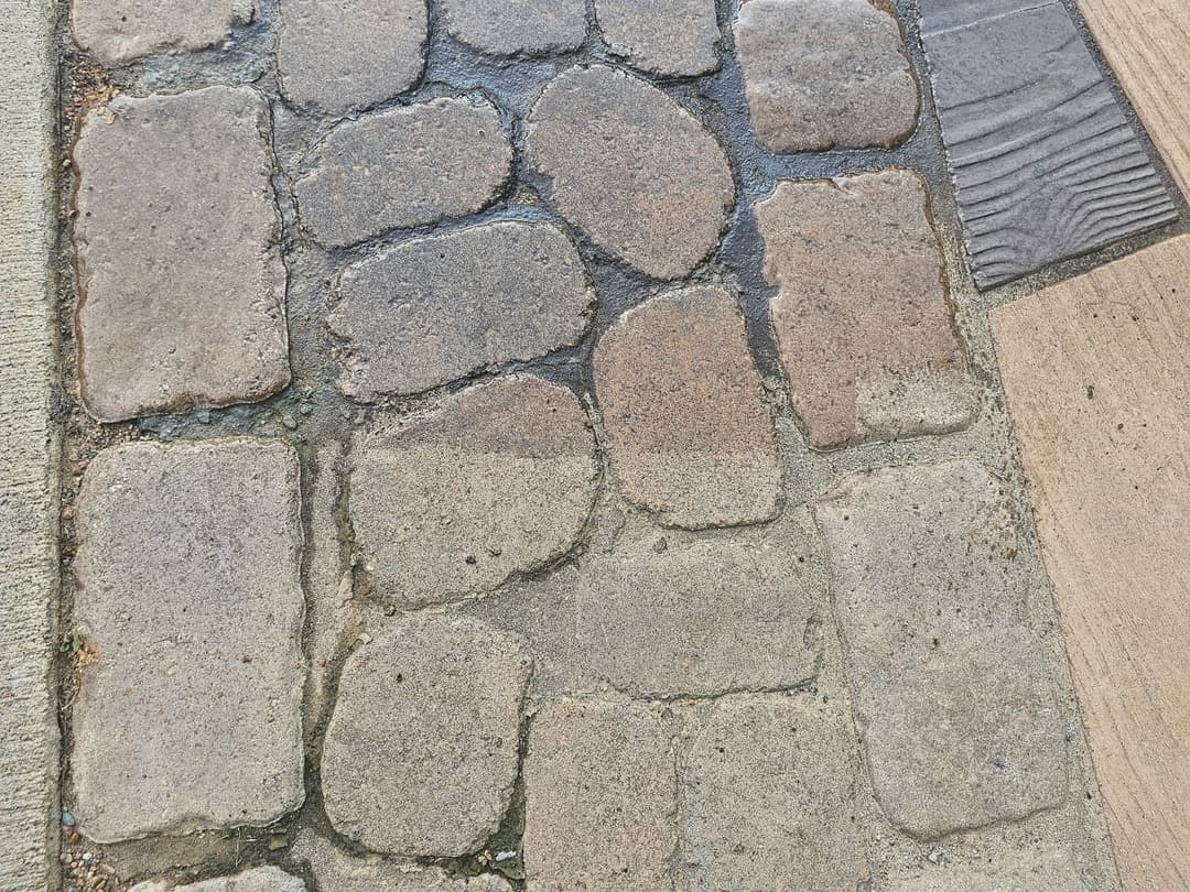 Textured stone and concrete pavement with wet cobblestones in urban setting.