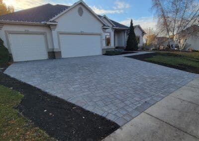 Paver stone driveway in front of a modern house with two garages and landscaped yard.