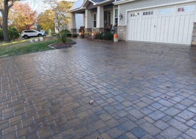 Paved driveway with decorative bricks in front of a house and autumn landscaping.