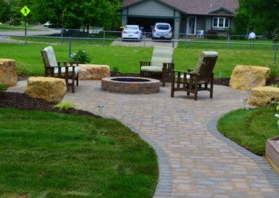 Cozy outdoor fire pit area with wooden chairs and natural stone seating in a landscaped yard.