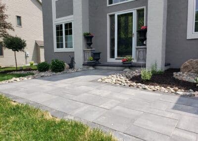 Modern house entrance with pavers, planters, and landscaped stone features.