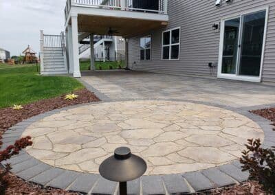 Patio with circular stone design, landscaped yard, and modern home exterior.