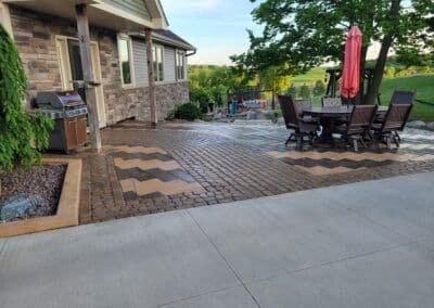 Outdoor patio with a grill, dining set, and stylish stone pavers surrounded by greenery.