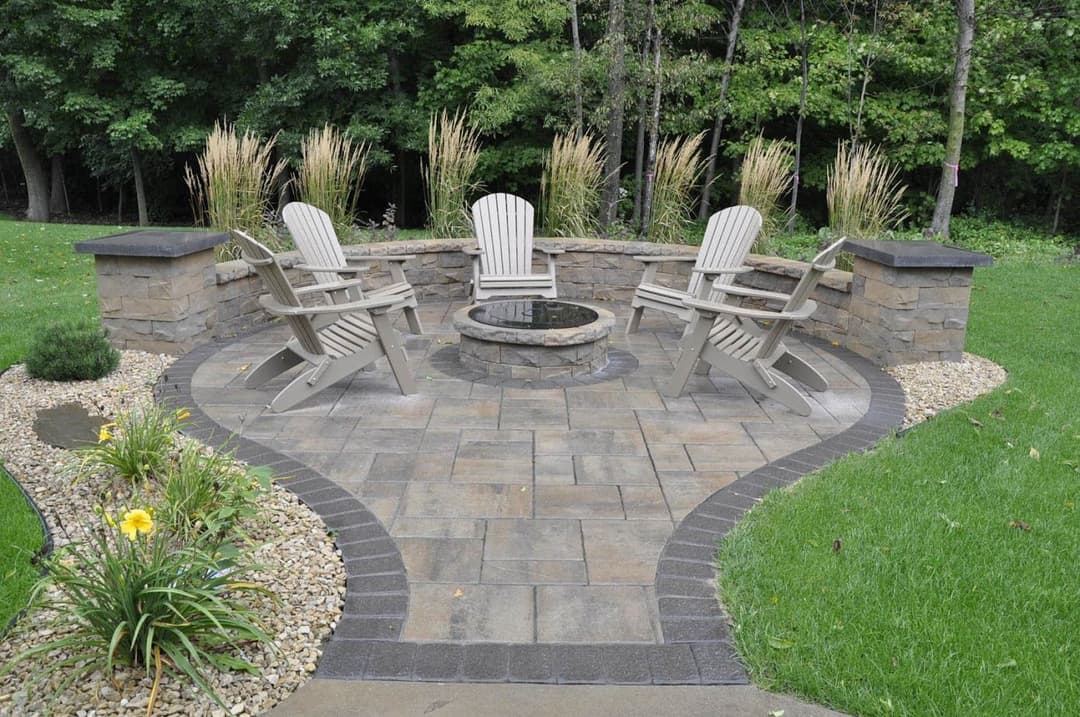 Patio seating area with stone fire pit, surrounded by greenery and decorative landscaping.