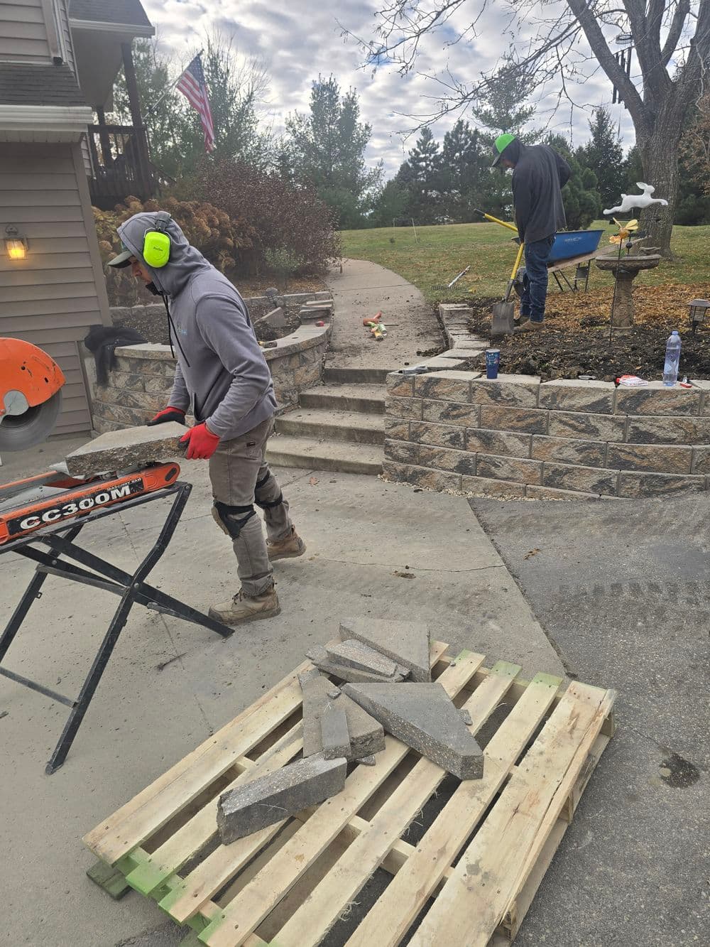 Workers installing stone retaining wall outdoors with tools and materials on-site.