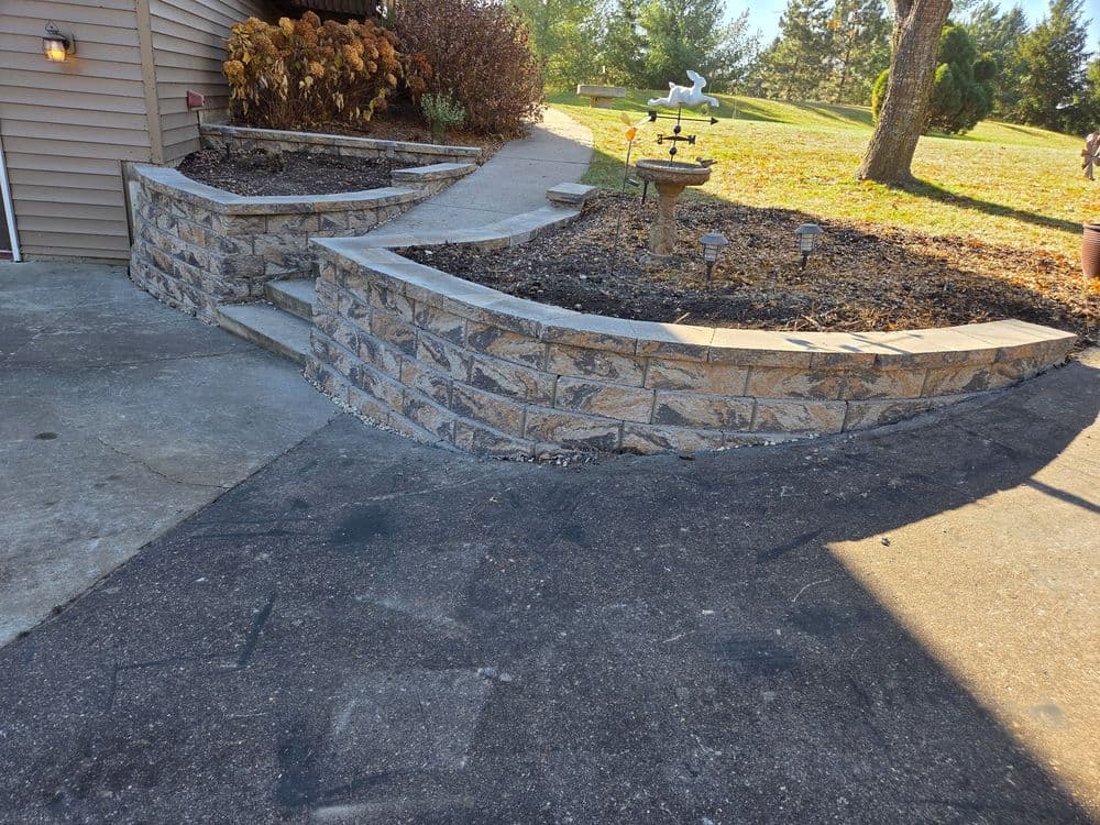 Landscaped stone retaining wall with pathway and decorative birdbath in a yard setting.